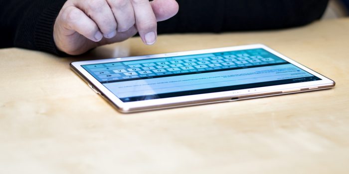 En hand pekar på en surfplatta som visar ett tangentbord.
