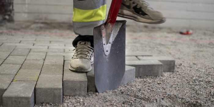 En person gräver med en spade i grus och lägger stenplattor