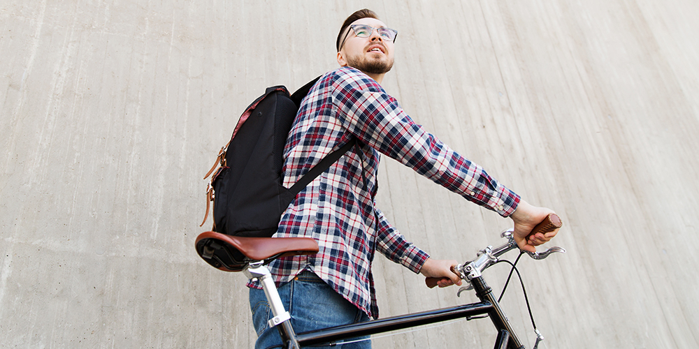Person med ryggsäck på ryggen leder en cykel.
