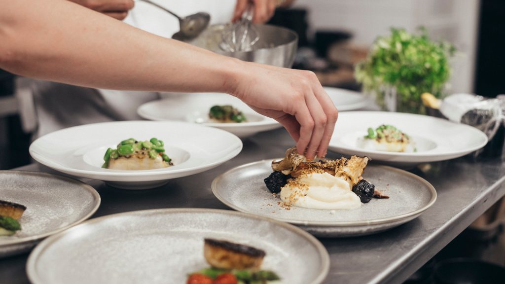 Personer som lägger upp mat på tallrikar i ett restaurangkök
