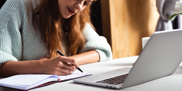 Rödhårig kvinna skriver och studerar på en bärbar dator.