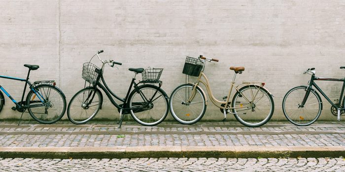 Fyra cyklar står lutade mot en husvägg.