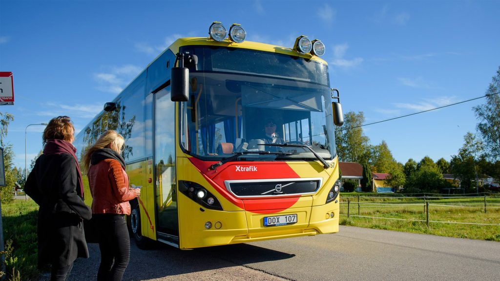 Två personer som står vid en busshållsplats och ska kliva på en buss