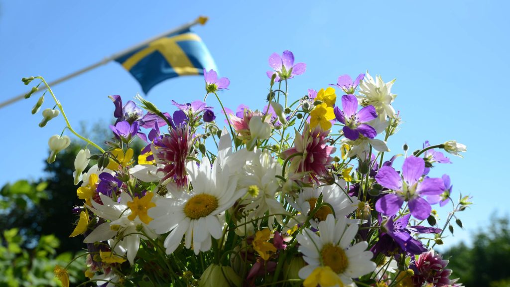 Midsommarkrans med svenska flaggan i bakgrunden