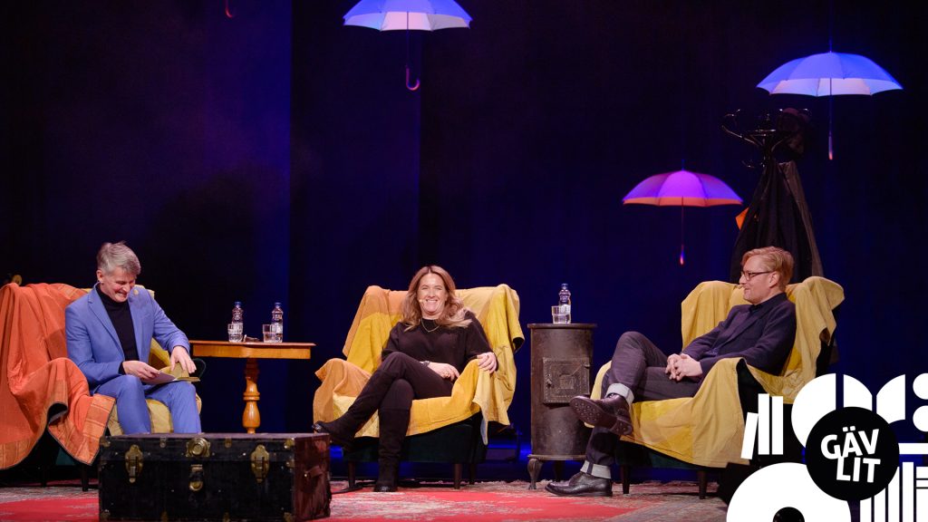 Tre författare på en scen under paraplyer