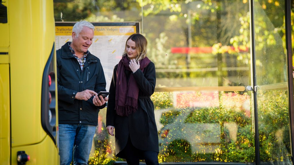 Två personer vid en busshållsplats.