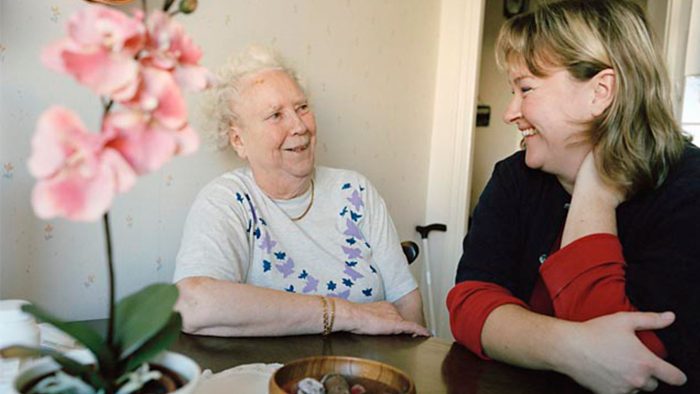 En äldre kvinna sitter tillsammans med en yngre kvinna vid ett bord och skrattar