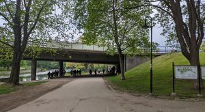 Gång- och cykelvägen som går under Kvarnbron. Lövträd och Gavleån syns i bakgrunden. Flera människor vandrar i området.