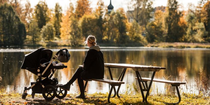 EN kvinna som sitter på en bänk och har en barnvagn till vänster om sig