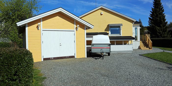 Gul villa med garage och en släpvagn som står utanför.