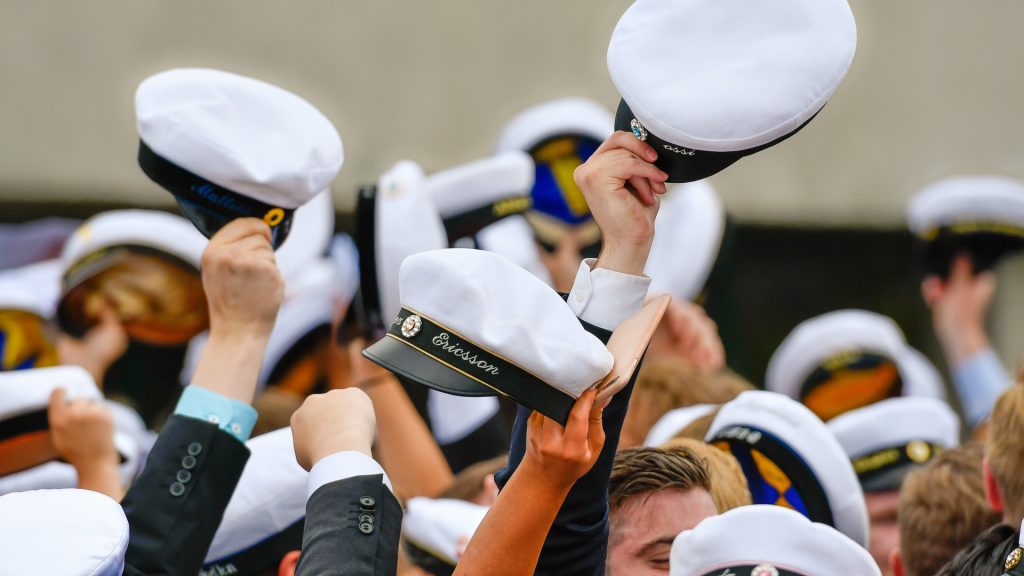 Händer som räcker upp studentmössor i luften.