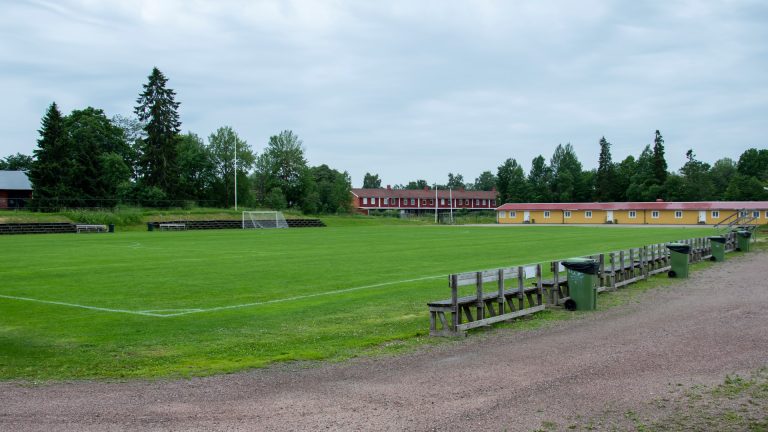 Brynäsvallens fotbollsplan med låg läktare i trä.