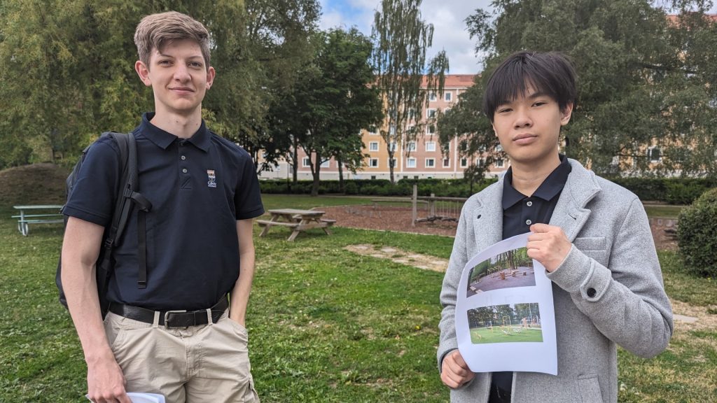 Två unga killar står och tittar in i kameran i en grönskande park
