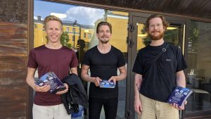 Tre män som står framför Förvaltningshusets entré med flyers i händerna