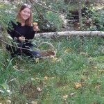 En kvinna sitter hukad is kogen och håller upp en kantarell