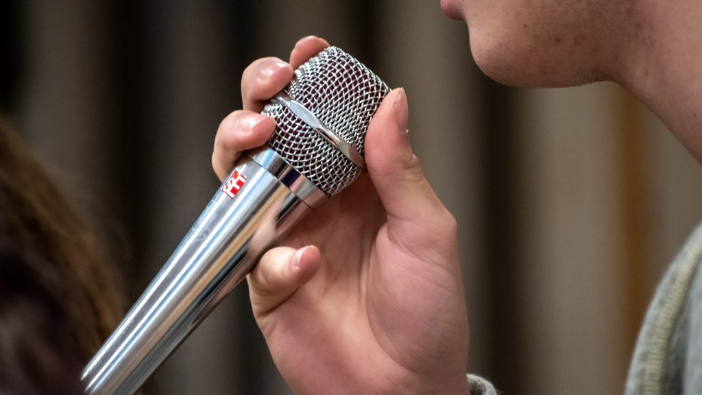 En hand som håller i en mikrofon intill en mun