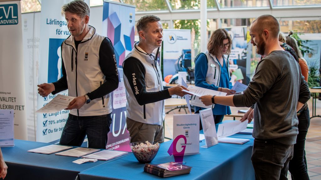 Personer står i en monter och delar ut och tar emot broschyrer