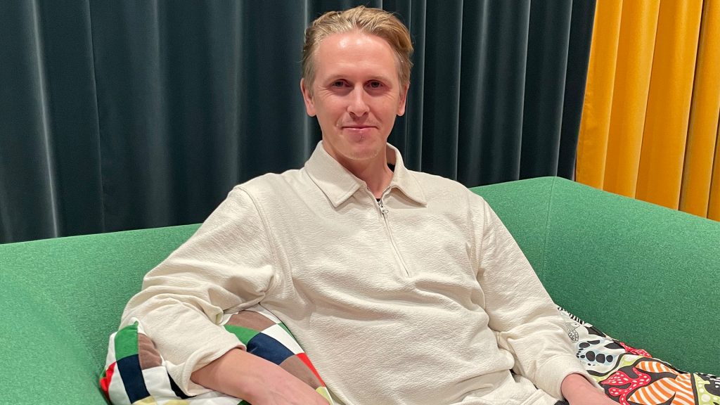 En man med blont hår sitter i en grön soffa.