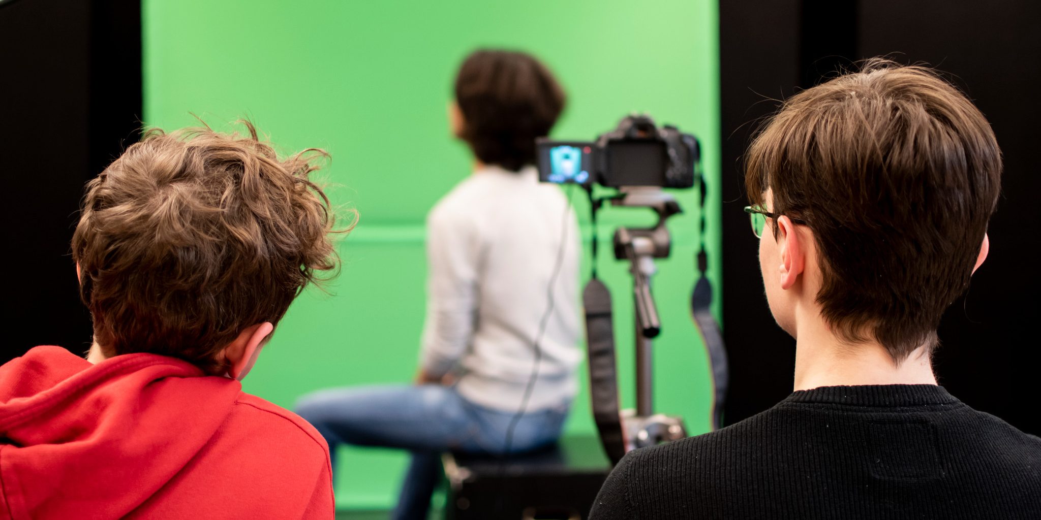 Tre elever står i en studio med en grön bakgrund. En kamera filmar en person.