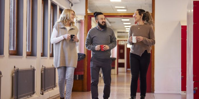 Lärare går i en skolkorridor med kaffekopp i händerna.