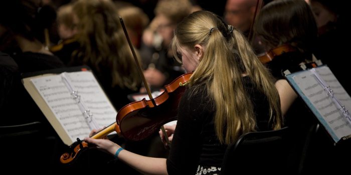 En person i undre tonåren spelar fiol på en konsert.
