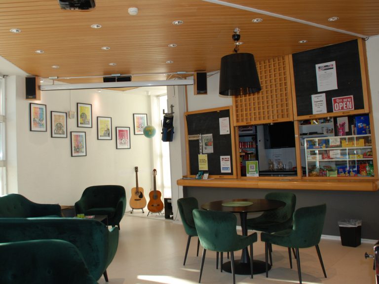 Ett cafe med stolar och bord. I bakgrunden skymtar gitarrer och tavlor.