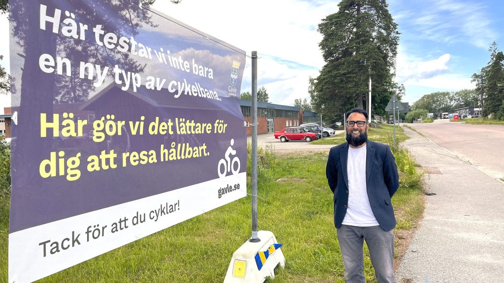 Amer Aslam står bredvid en banderoll om hållbart resande