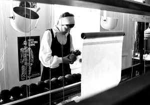 Svart-vitt fotografi på Maria Adlercreutz med garn i handen framför en vävstol.