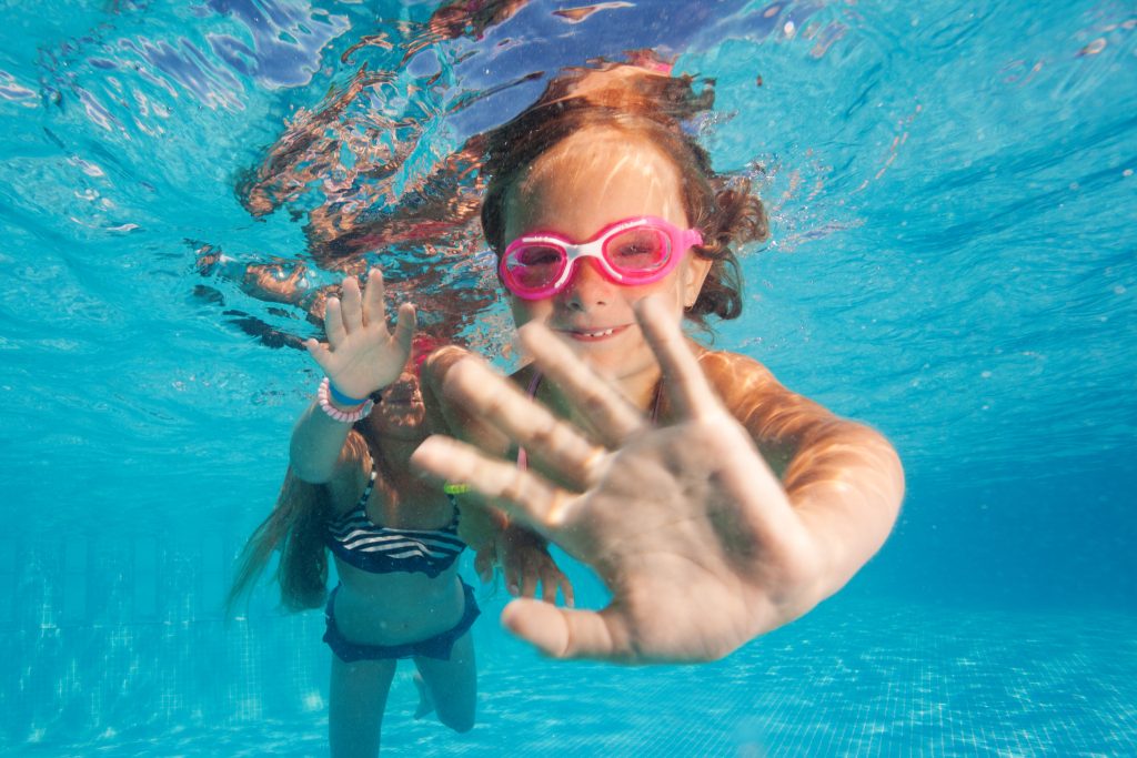Två tjejer som dyker under vatten i en pool