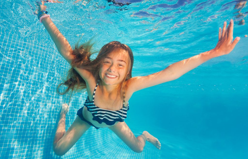 Flicka som dyker under vatten i en pool