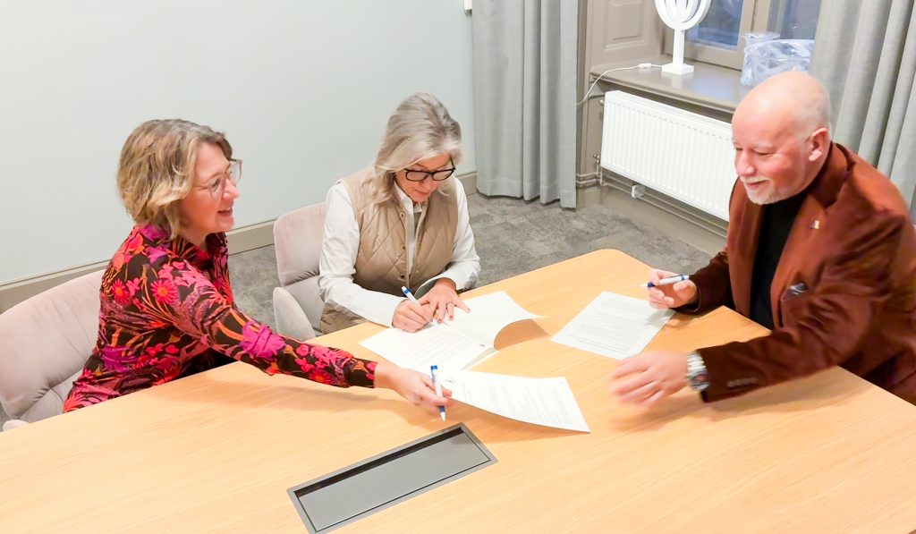 Två kvinnor och en man som sitter vid ett bord och skriver samt skickar papper mellan varandra.