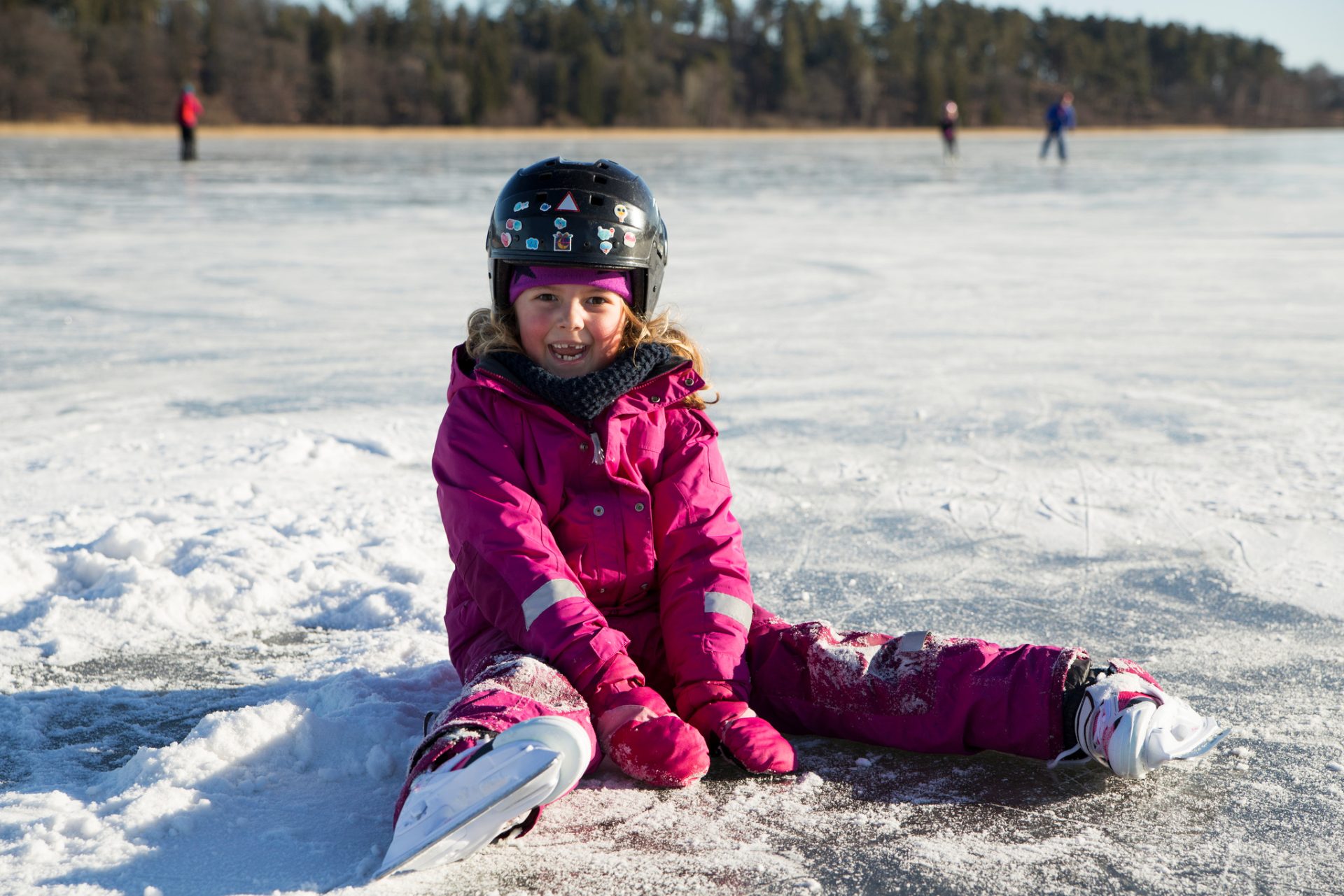 Flicka med hjälm och skridskor sitter på isen