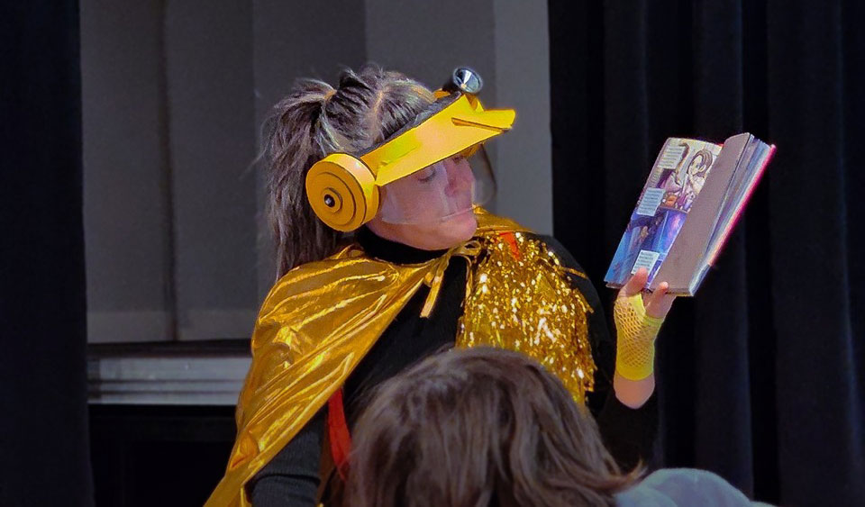 En person i gult och guldiga kläder läser ur en bok