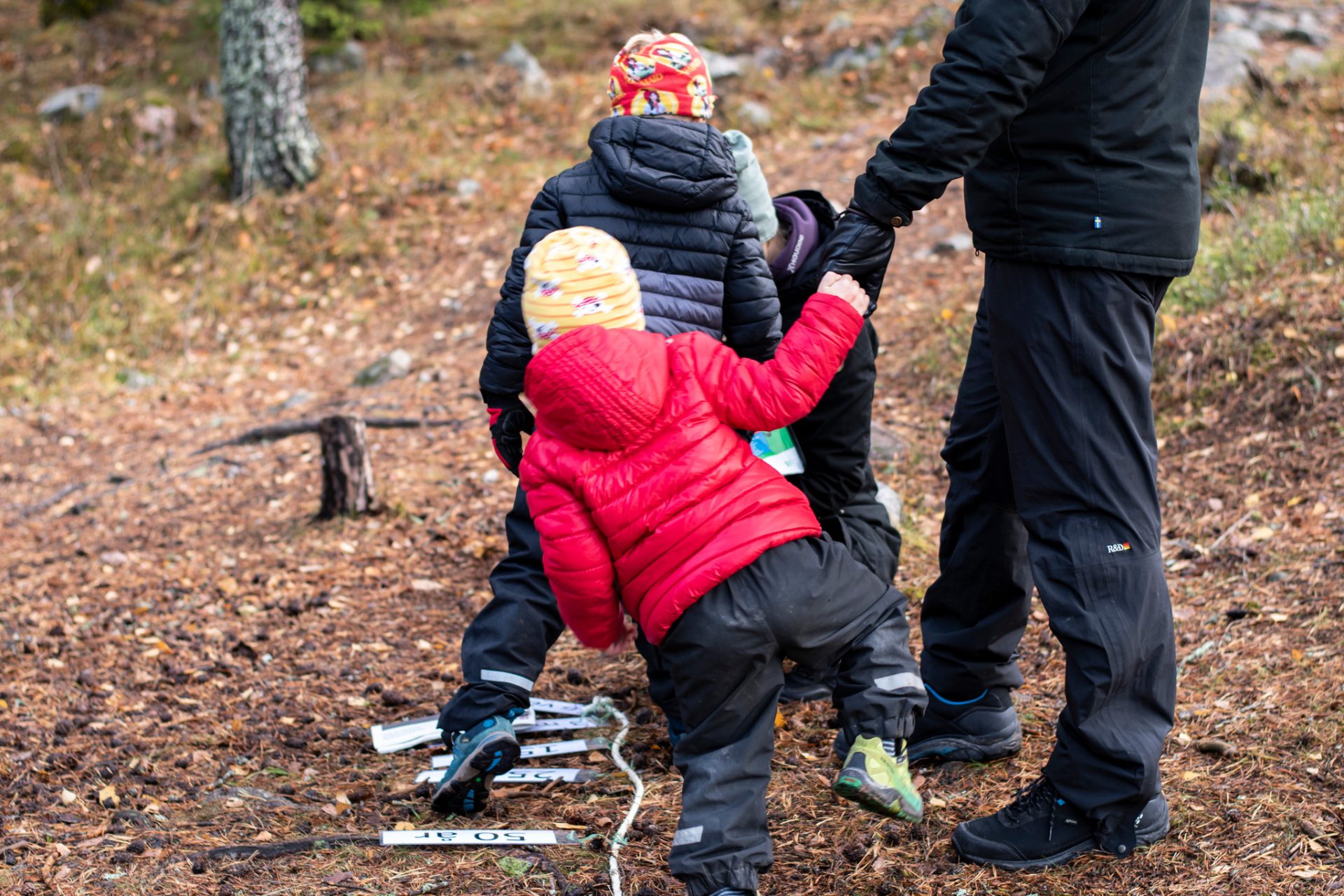 Två barn som leker med en vuxen i naturen.