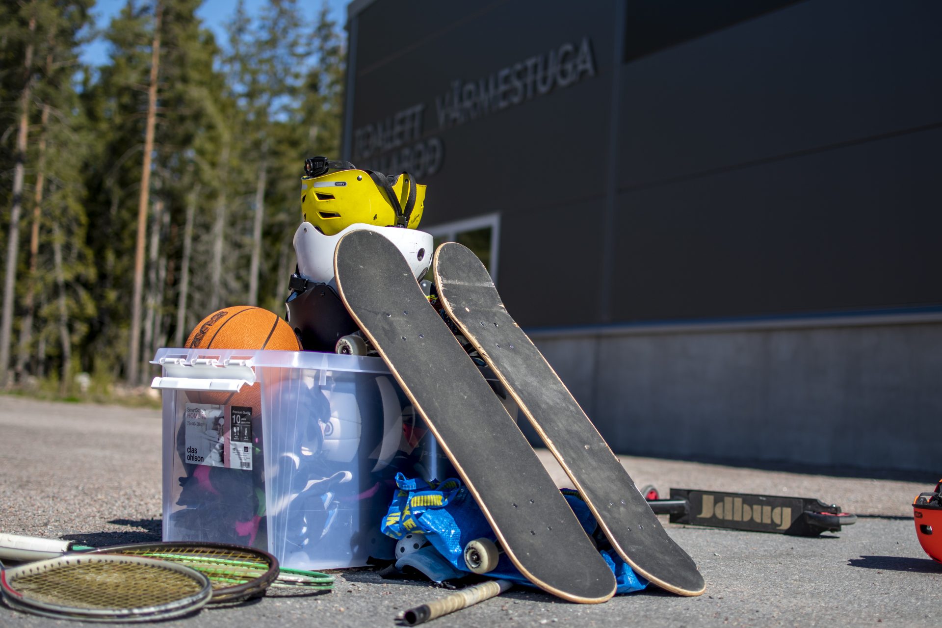 En skateboard, tennisracketar och annan sportutrustning ligger på marken.