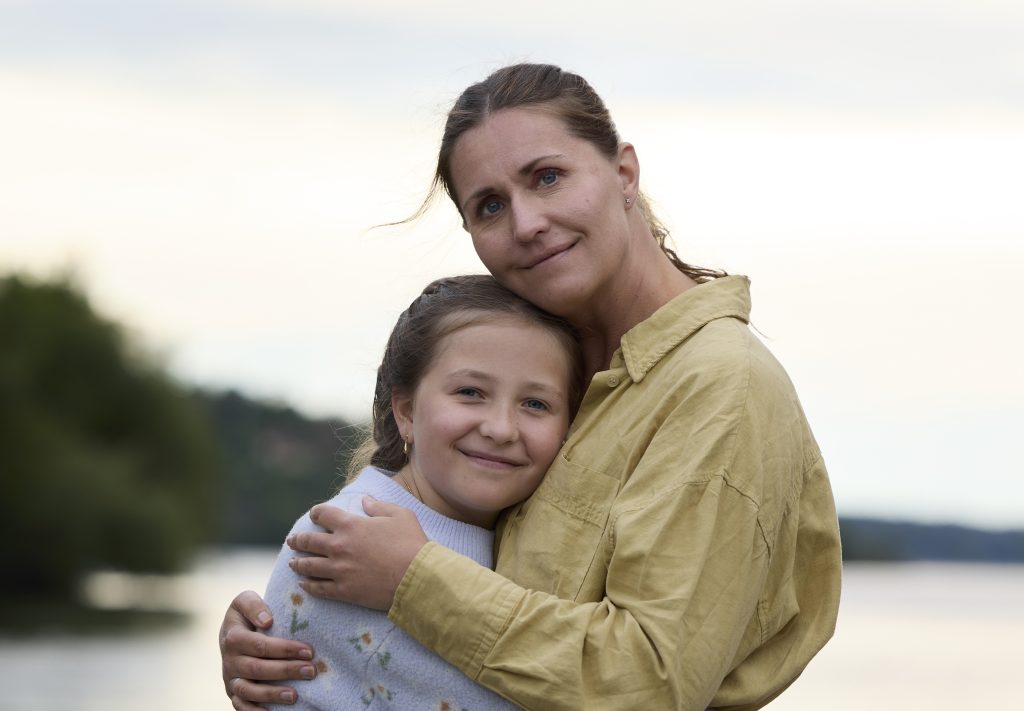 En mor och dotter som kramar varandra vid vattnet.